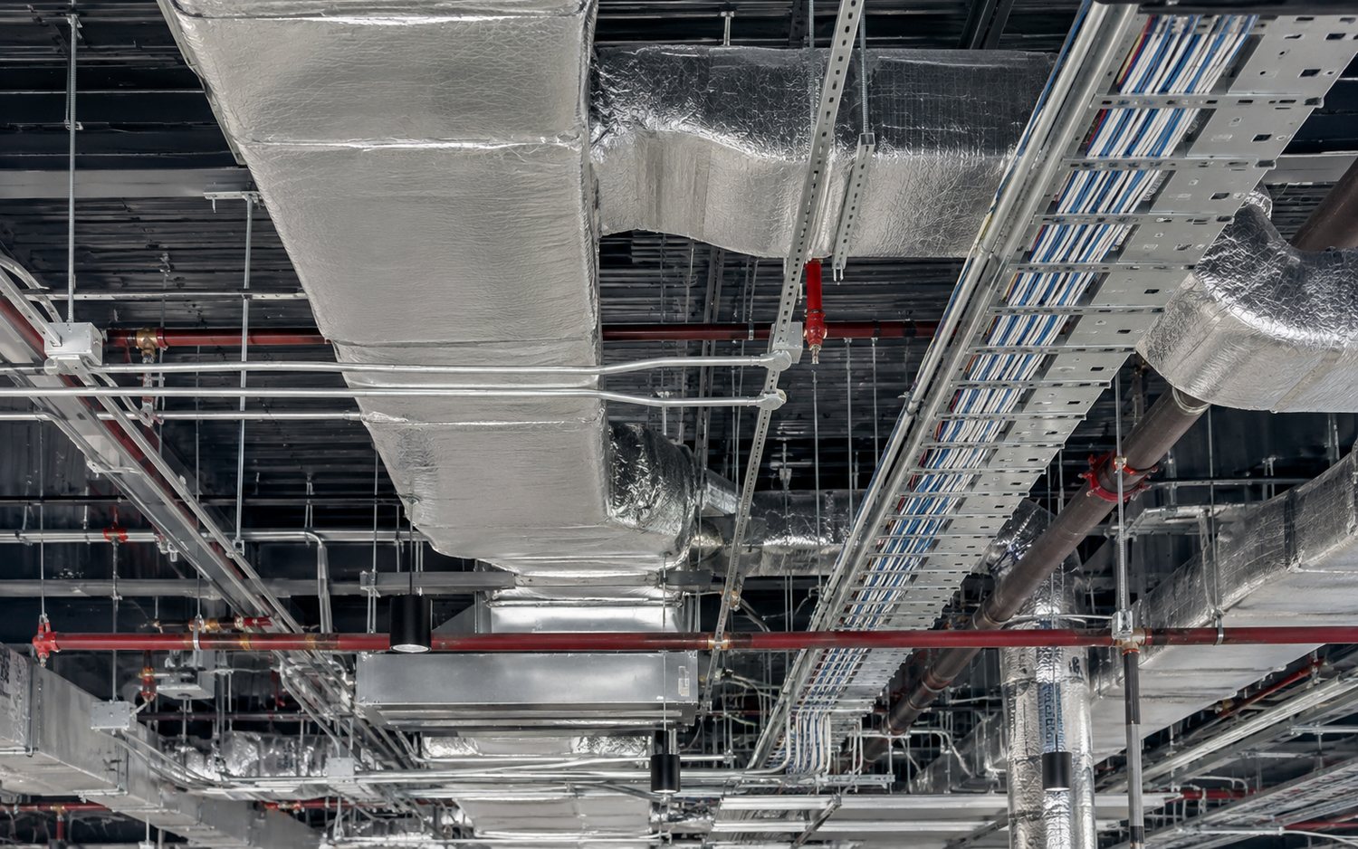 Above-ceiling plenum with insulated ductwork, sprinkler mains, cable tray and conduit sharing the same space